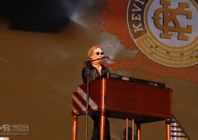 A musician wearing sunglasses plays a Korg keyboard on stage at the PNC Pavillion in front of a large Brotherhood of Rock logo.