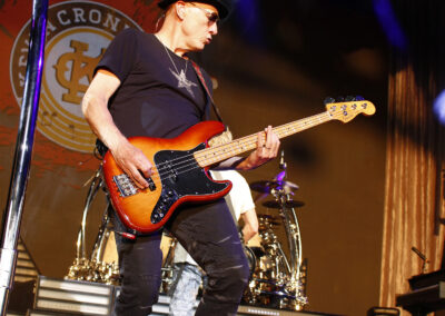 A man in a black hat and t-shirt plays a sunburst electric bass guitar on stage with the Kevin Cronin Band at the PNC Pavilion.