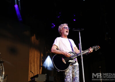 Kevin Cronin plays an acoustic guitar while performing on stage during the Brotherhood of Rock Tour.