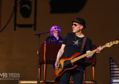 A bass player in a black t-shirt and fedora performs on stage at the PNC Pavilion next to a keyboardist during the Brotherhood of Rock Tour.