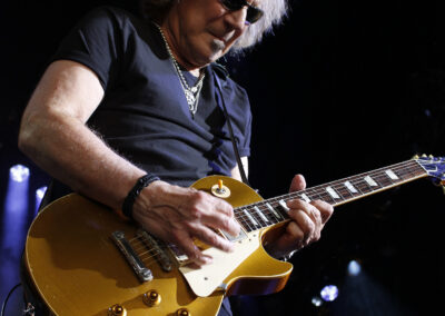 Musician in sunglasses plays a gold-top electric guitar on stage during the Brotherhood of Rock Tour.