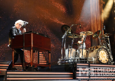 a keyboard at a PNC Pavilion concert while a drummer performs behind him on a stage with a sparkling backdrop.